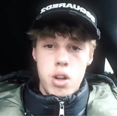 a young man wearing a hat and jacket in the back seat of a car with his mouth open