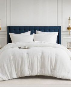 a bed with white linens and pillows in a room next to two lamps on either side of the bed