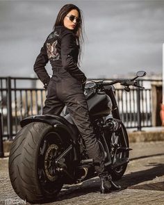 a woman in black riding on the back of a motor bike with her hands on her hips