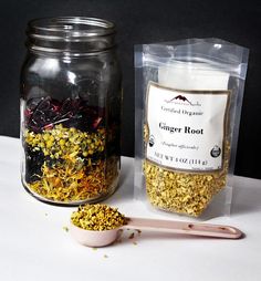 two jars filled with different types of flowers next to a spoon and bag of ginger root