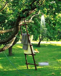 an outdoor shower is set up in the grass near a tree and buckets with towels on it