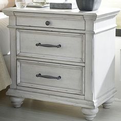 a white nightstand with two drawers and a vase on top