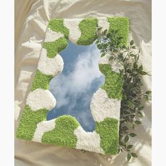 a green and white square shaped mirror sitting on top of a bed next to a plant