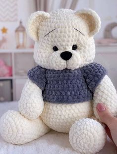 a crocheted white teddy bear sitting on top of a bed next to a person's hand