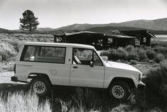 a black and white photo of a jeep parked in the middle of an open field