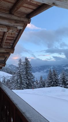 snow covered trees and mountains in the distance from a porch with wooden railings on it