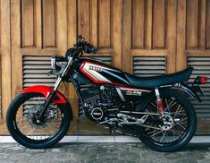 a red and black motorcycle parked in front of a wooden garage door with shutters