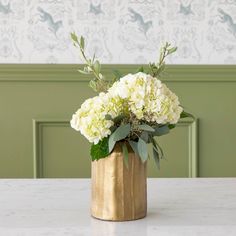 a gold vase filled with white flowers on top of a marble table next to a green wall