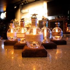 four glass bottles sitting on top of a wooden stand in front of a bar filled with liquor