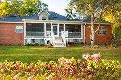 a brick house with white porches and flowers in the front yard