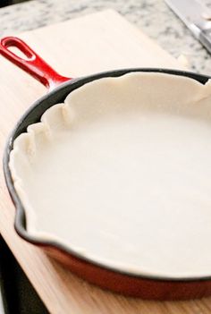 a skillet on a cutting board with a red handled spatula in the middle