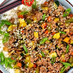 a white plate topped with meat and vegetables on top of rice next to chopsticks