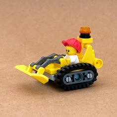 a yellow toy bulldozer with a red hat on it's head sitting on a brown surface