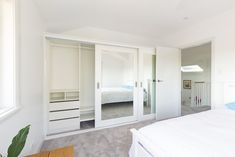 a bedroom with white walls and carpeted flooring has sliding glass doors to let in light into the room