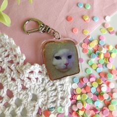 a white cat with blue eyes is on a pink keychain next to colorful sprinkles