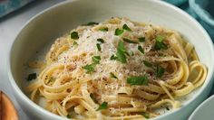 a white bowl filled with pasta topped with parmesan cheese and green herbs on top