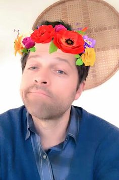 a man wearing a straw hat with flowers on it's head and looking up