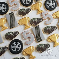 cookies decorated with gold and black cars, tires, and cupcakes are displayed on a white table