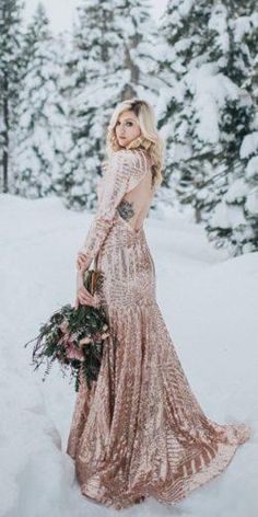 a woman standing in the snow wearing a long dress and holding a bouquet with flowers