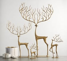 three gold deer statues standing in front of a white wall and wrapped presents on the floor