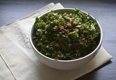 a white bowl filled with green vegetables on top of a wooden table next to a napkin