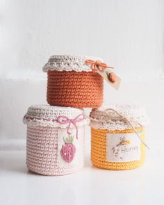 three crocheted jars with labels on them sitting side by side in front of a white background