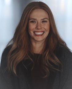 a woman with long brown hair smiling at the camera while wearing a black jacket and white shirt