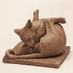 a sculpture of a cat laying on top of a piece of wood with it's tail curled up