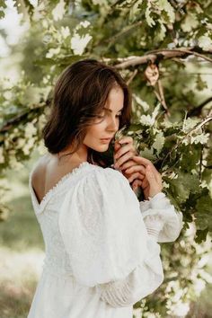 a woman in a white dress is standing under a tree and looking at the camera