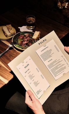 a person sitting at a table with some food on top of it while holding up a menu