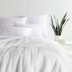 a bed with white sheets and pillows next to a potted plant