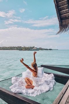 a woman sitting on top of a boat in the ocean with her arms raised up