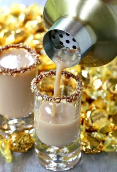 two glasses filled with liquid next to gold confetti and a shaker being poured into them