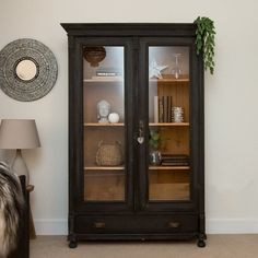 a black china cabinet with glass doors and shelves in the corner next to a lamp