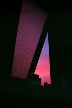 the sun is setting behind some buildings in the dark, with pink and blue colors