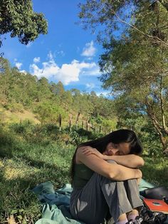 a woman sitting on top of a blanket next to trees