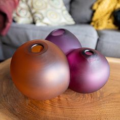 three purple and brown vases sitting on top of a wooden table next to a gray couch