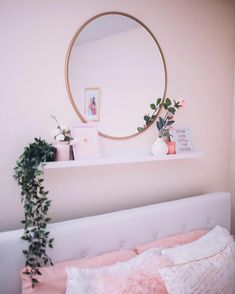 a bed with pink sheets, pillows and a round mirror on the wall above it