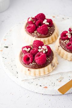 raspberry and chocolate tarts on a white plate with a gold serving utensil