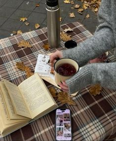 a person sitting on a bench with an open book and cup of tea in their hands