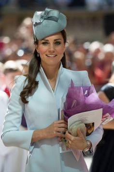 a woman in a blue coat and hat holding a purple bouquet while standing next to other people