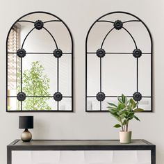 two mirrors on the wall above a table with a potted plant next to it