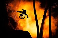 a person on a dirt bike in the air above some trees and fire behind them