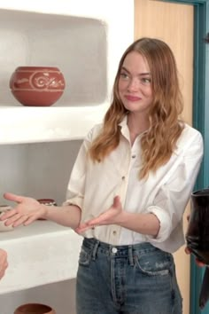 a woman standing in front of a shelf holding her hands out to someone behind it