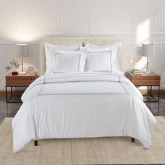 a bed with white sheets and pillows on top of it in a bedroom next to two nightstands