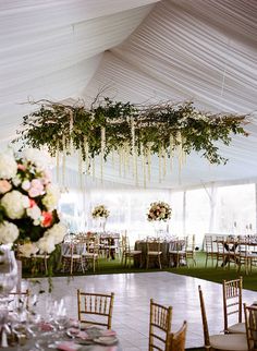 the inside of a tent with tables, chairs and flowers hanging from it's ceiling