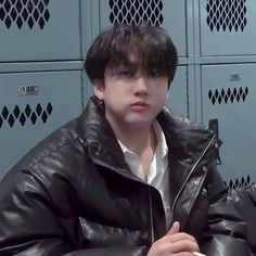 a young man sitting in front of lockers wearing a black leather jacket and white shirt