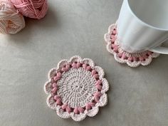 two crocheted coasters sitting on top of a table next to a cup