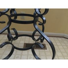 a metal table with an iron design on the top and bottom, in front of a beige wall