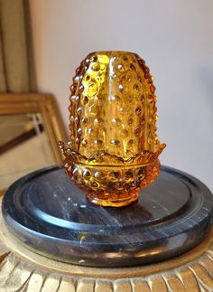 a yellow glass vase sitting on top of a metal stand in front of a mirror